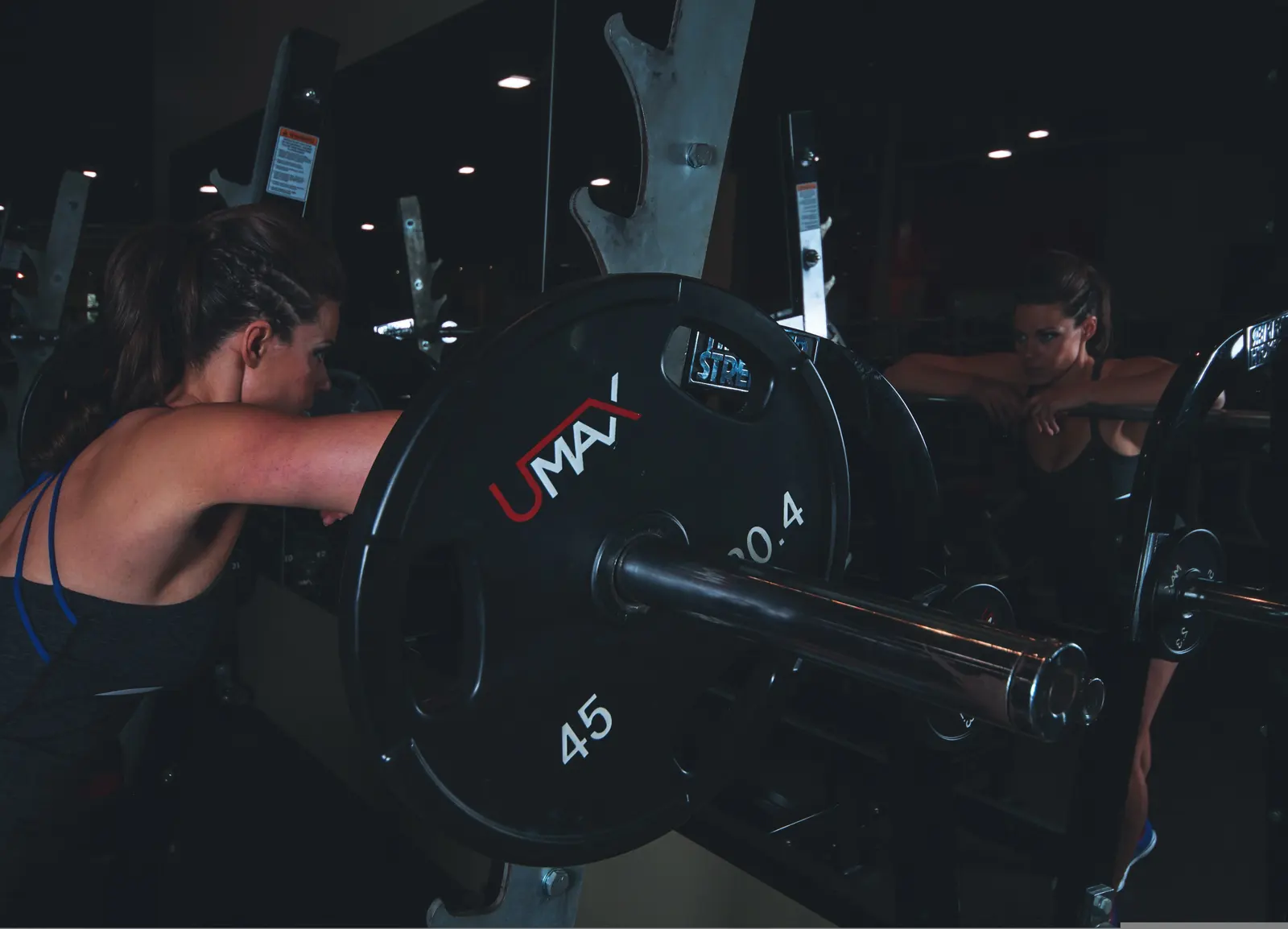 En kvinna vilar armarna på skivstången i stället, i ett mörkt gym